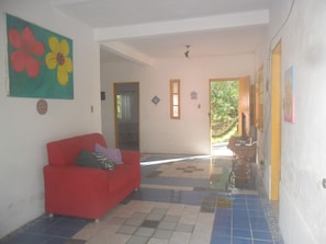 A hallway with a red sofa, a colorful flower painting, and a tiled floor.
