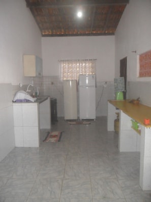 A compact kitchen with a tiled floor, a sink, a cabinet, two refrigerators, and a window with curtains.