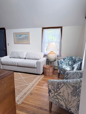A living room with a sofa, a patterned armchair, a lamp, and a framed picture on the wall.