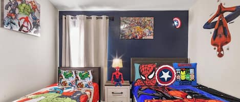 A child's bedroom with two beds, superhero-themed bedding, a Spider-Man pillow, and wall art.