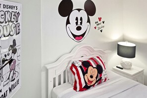 Ein Kinderzimmer mit Wandsticker von Mickey Mouse, einem Poster mit Mickey Mouse und einem Mickey-Motiv-Kissen auf dem Bett.
