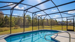 A swimming pool with a metal frame and glass panels, surrounded by a metal fence, with a view of trees and houses in the background.