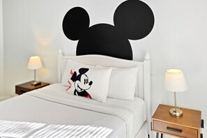 A bed with a Mickey Mouse headboard, a pillow with Mickey Mouse, a bedside lamp, and a nightstand with a lamp. - 5 Beds - Private Pool - 15 Mins to Theme Parks (Davenport)