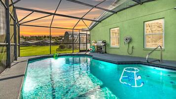 Une piscine avec vue sur le coucher de soleil, un barbecue et un tuyau d’arrosage.