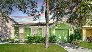 A single-story house with a green garage, a well-maintained lawn, and a tree in the front yard.
