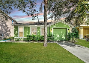 A single-story house with a green garage, a well-maintained lawn, and a tree in the front yard.