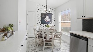 A kitchen with white cabinets, a marble floor, a dining table with chairs, a dishwasher, and a window with blinds.