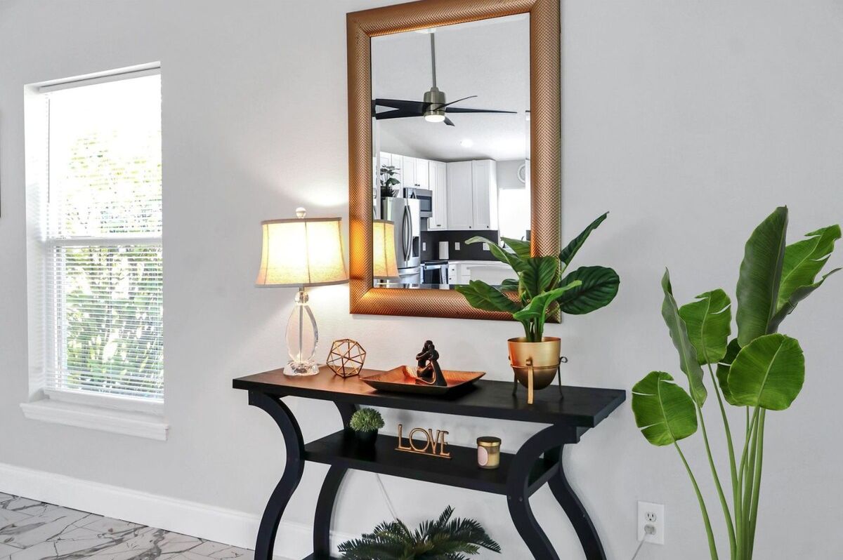 Une pièce comprenant une console, un miroir, une lampe, une plante en pot et un objet décoratif portant le mot « AMOUR ».