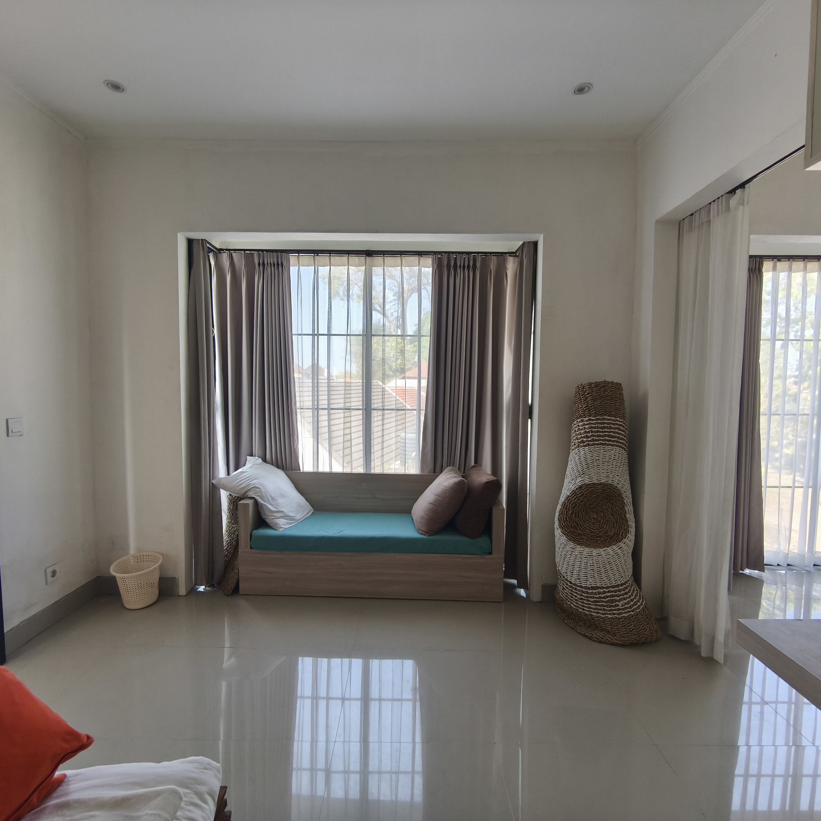 A room with a built-in bench, a woven basket, and a large window with curtains.