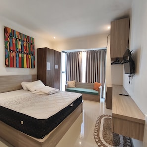 A modern bedroom with a large bed, a sofa, a TV, and a colorful painting on the wall. - OYO 95416 Griya House Bstc (Bali)