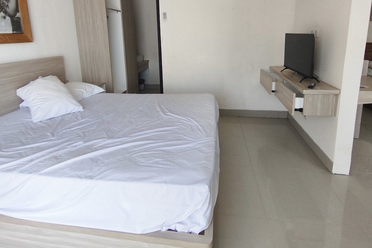 A bedroom with a bed, a TV on a shelf, and an air conditioning unit.