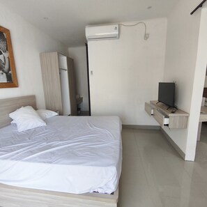Una camera d'albergo con un letto, una televisione su una mensola in legno e un condizionatore d'aria a parete.