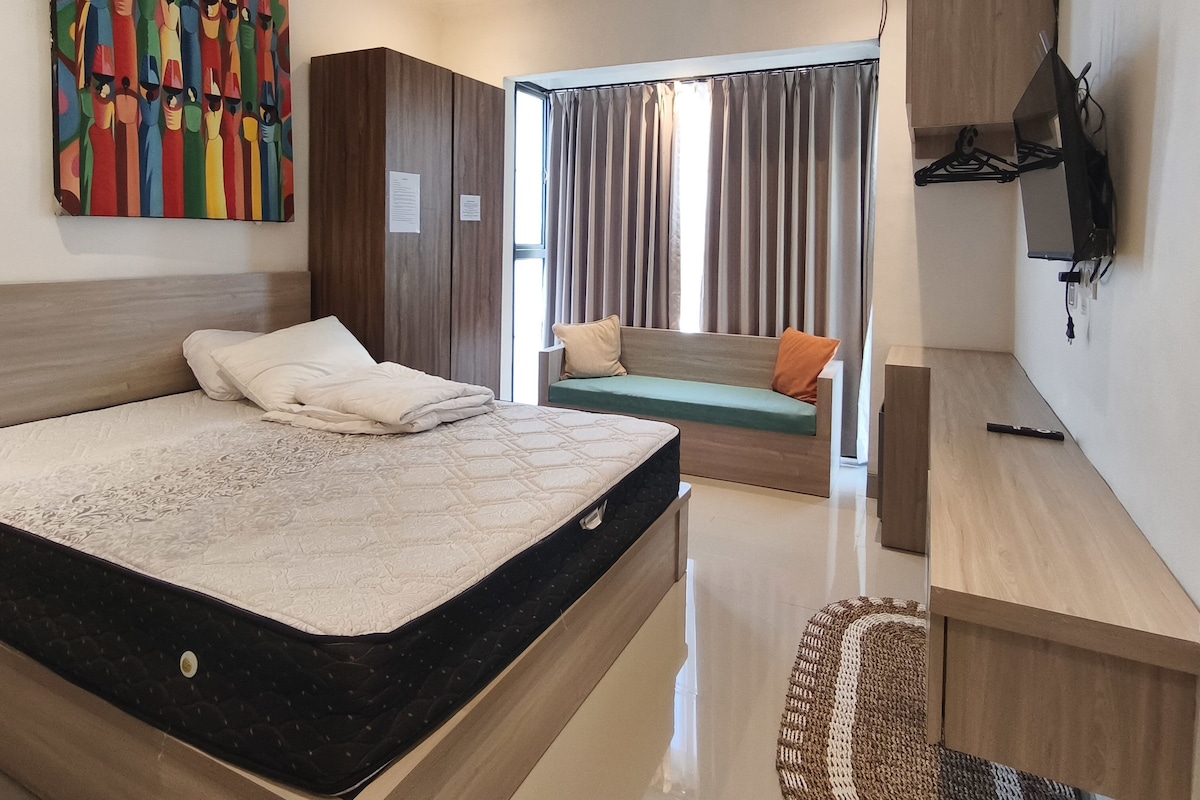 A modern bedroom with a large bed, a sofa, a desk, and a colorful abstract painting.