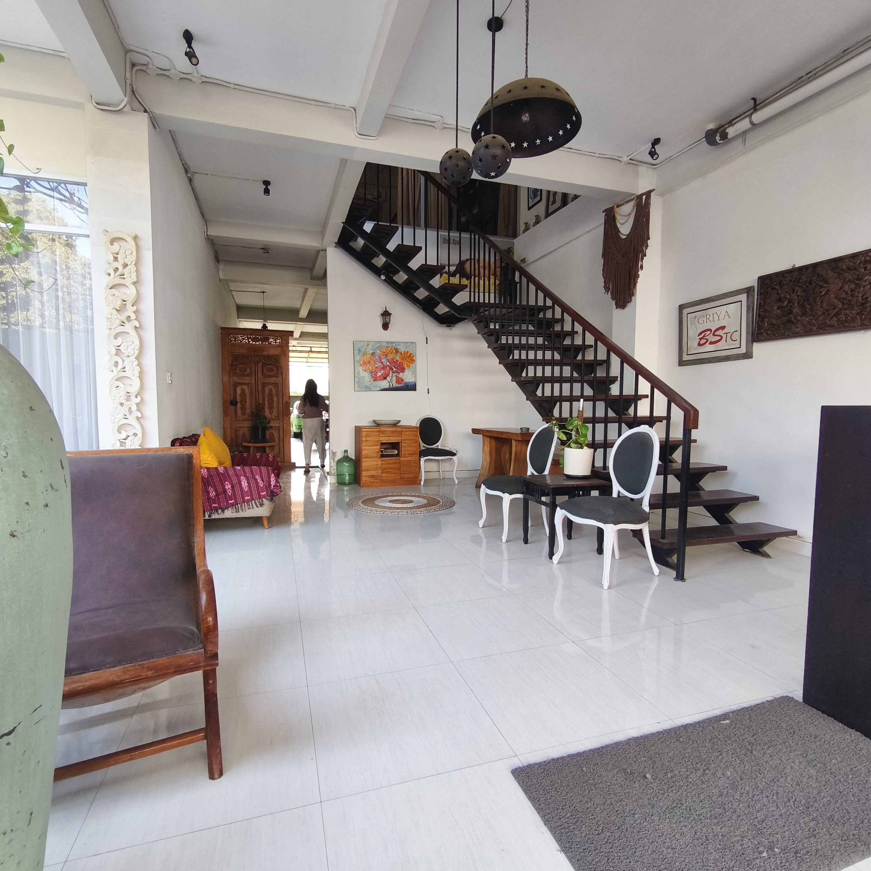 Ampla sala de estar com escada, sofá, mesa de jantar e cadeiras, além de um objeto decorativo na parede.