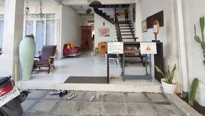 Área de entrada coberta com escadaria, placa de boas-vindas e sinalização de estacionamento.