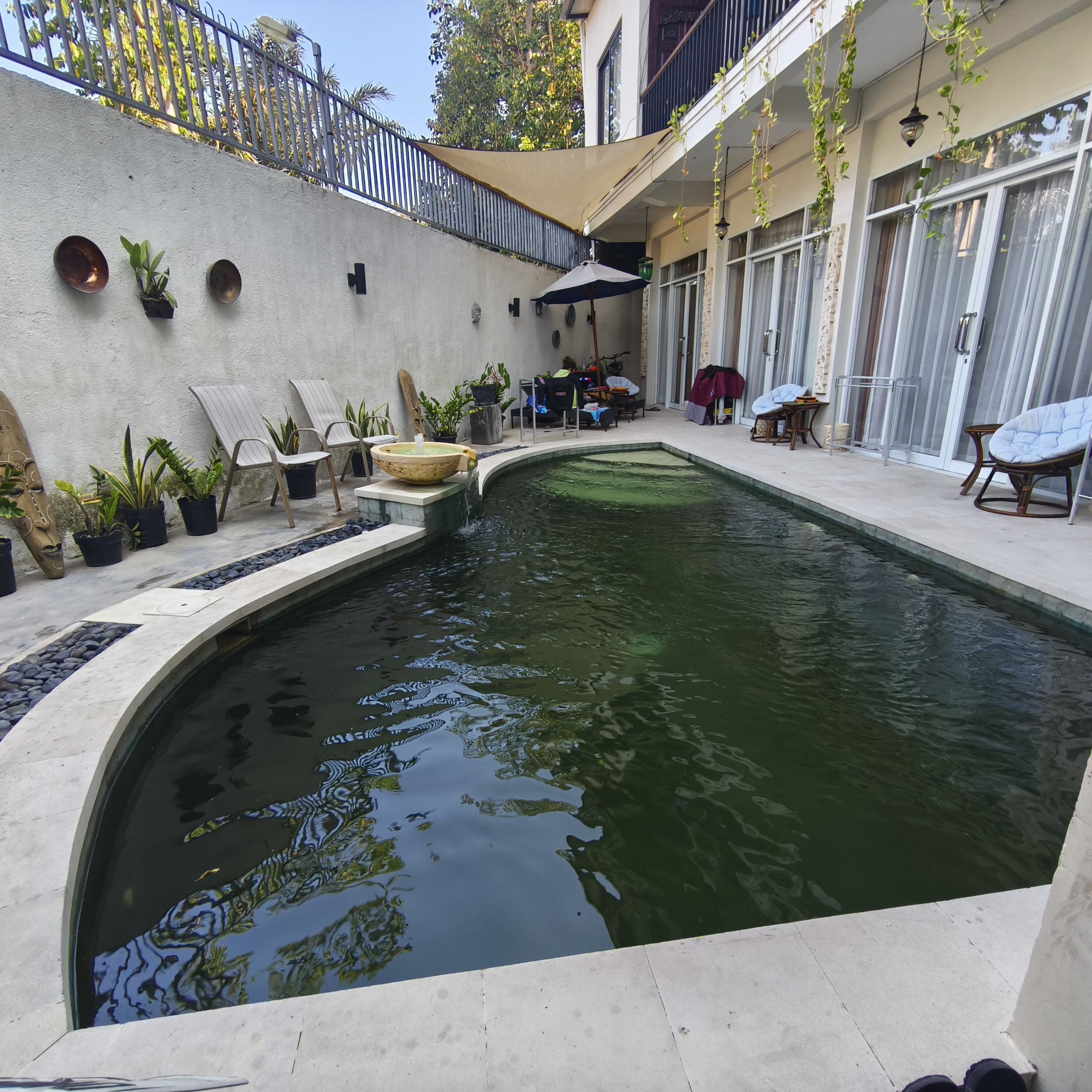 Piscina com borda de pedra, rodeada por espreguiçadeiras e plantas em vasos.