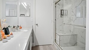 Une salle de bain moderne avec un plan de toilette blanc, une douche en verre et une porte dotée d’un porte-serviettes.