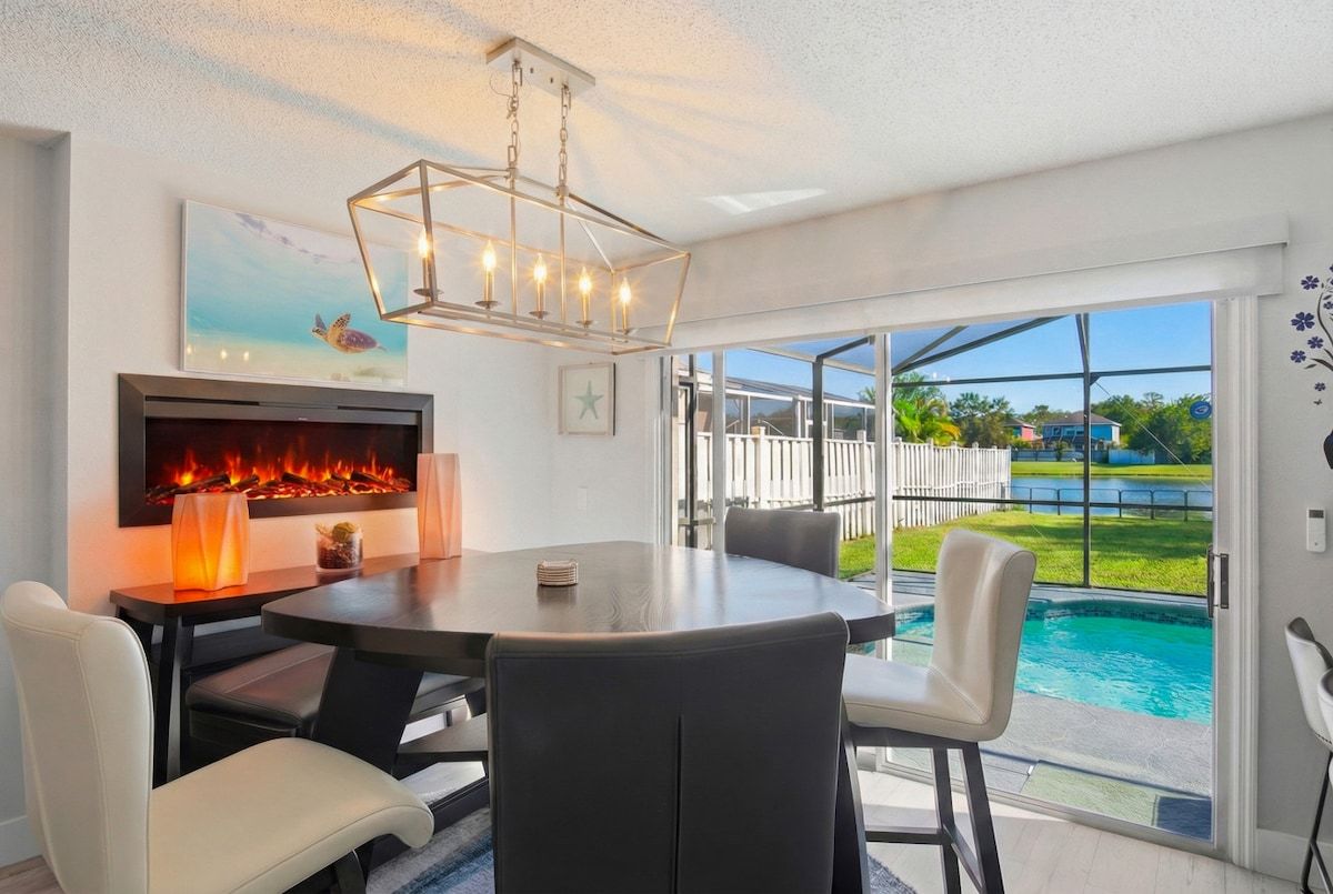 A dining area with a round table, chairs, a fireplace, and a view of a swimming pool.