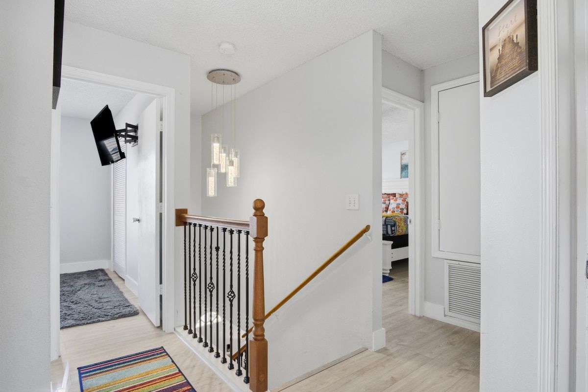 Ein Flur mit einer Holztreppe, einer schwarzen Wandleuchte und einem gemusterten Teppich.