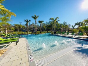 Une piscine agrémentée d’une fontaine, entourée de palmiers et de chaises longues vertes.