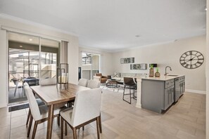 A modern kitchen with a central island, a dining area with a wooden table and chairs, and a living area with sofas and a coffee table. - King Bed | Disney Contemporary Townhouse (Kissimmee)