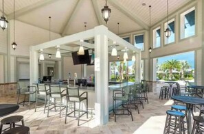 An indoor dining area with multiple tables and chairs, a bar counter, and a flat-screen TV mounted on the wall. - King Bed | Disney Contemporary Townhouse (Kissimmee)