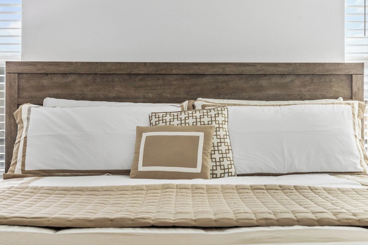 Un lit avec une tête de lit en bois, une literie blanche et des coussins à motifs.