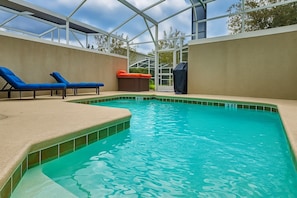 Een zwembad met blauwe ligbedden, een jacuzzi en een overdekt gedeelte.