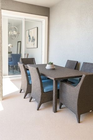 A dining area with wicker furniture and a glass door leading to a balcony. - Modern Orlando getaway near Disney & Universal! (Davenport)