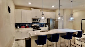 A modern kitchen with white cabinets, a large island with bar stools, stainless steel appliances, and pendant lighting. - Modern Orlando getaway near Disney & Universal! (Davenport)
