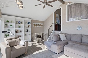 A modern living room with a sofa, a chair, a ceiling fan, and a bookshelf filled with decorative items. - Lakefront Paradise with 4 Decks and Unmatched Panoramic Views! (Sunrise Beach)