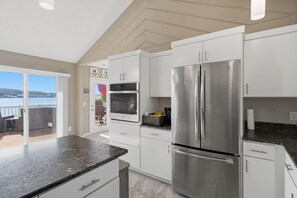 A modern kitchen with white cabinets, a stainless steel refrigerator, and a large window overlooking a scenic view. - Lakefront Paradise with 4 Decks and Unmatched Panoramic Views! (Sunrise Beach)