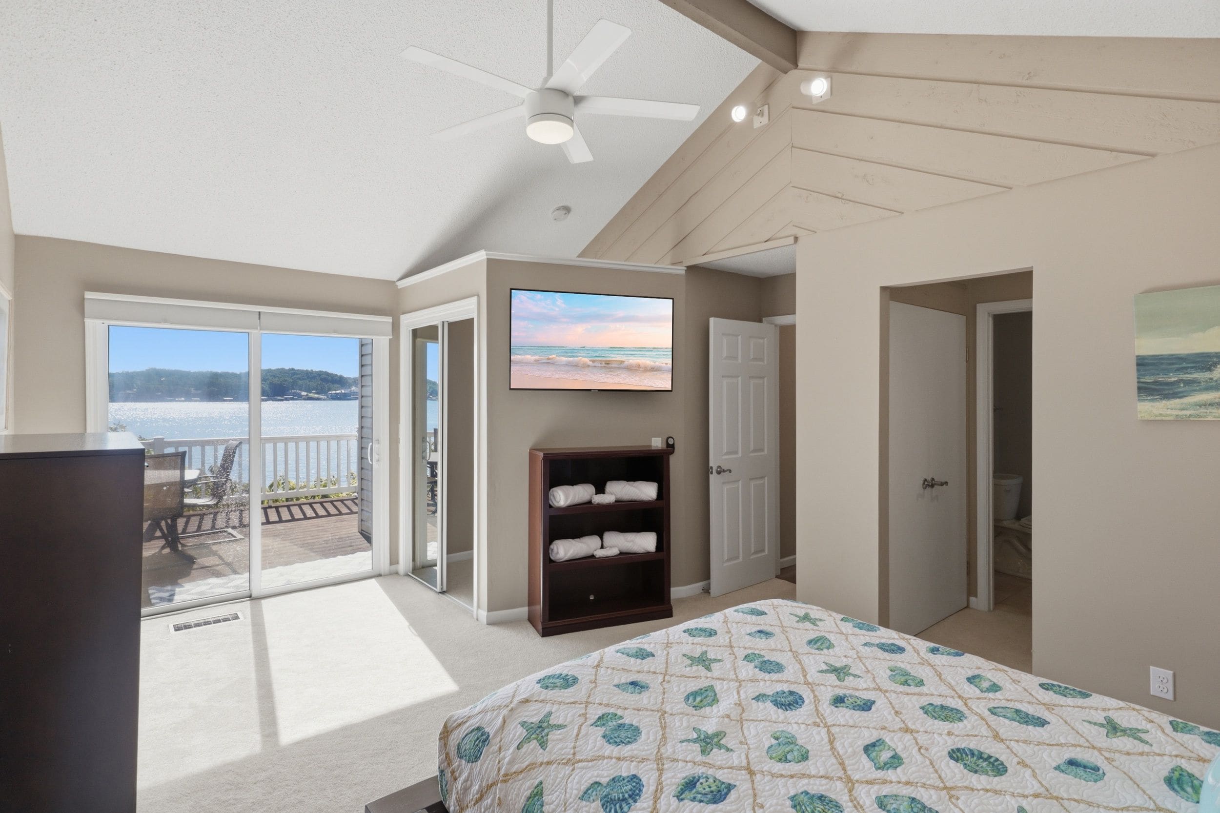 A bedroom with a bed, a ceiling fan, a TV, and a view of the outdoors.