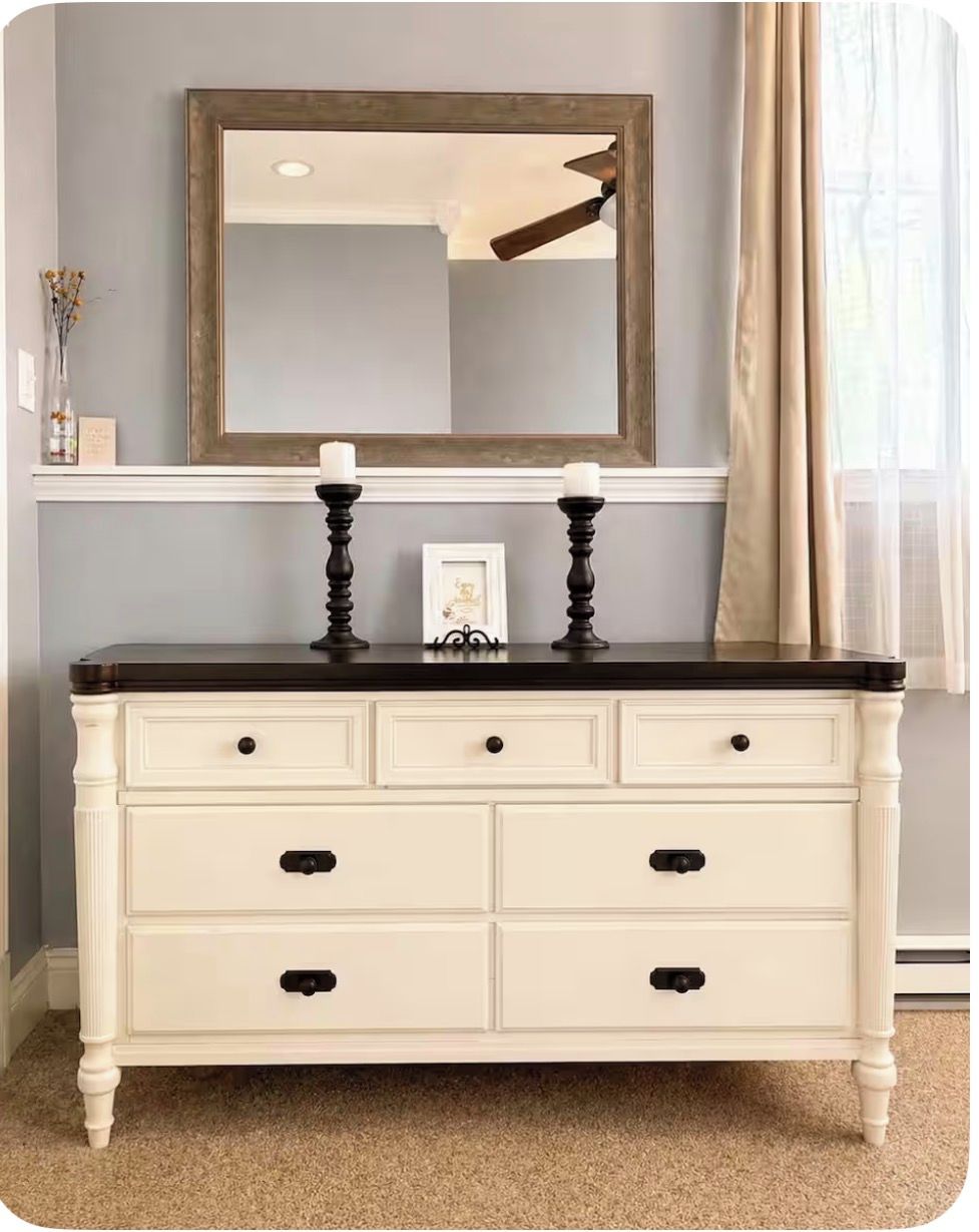 A white dresser with black handles, a mirror above it, and a candle on top.