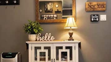 A room with a white cabinet, a mirror, a 'hello' sign, a lamp, and a 'New York' sign on the wall.