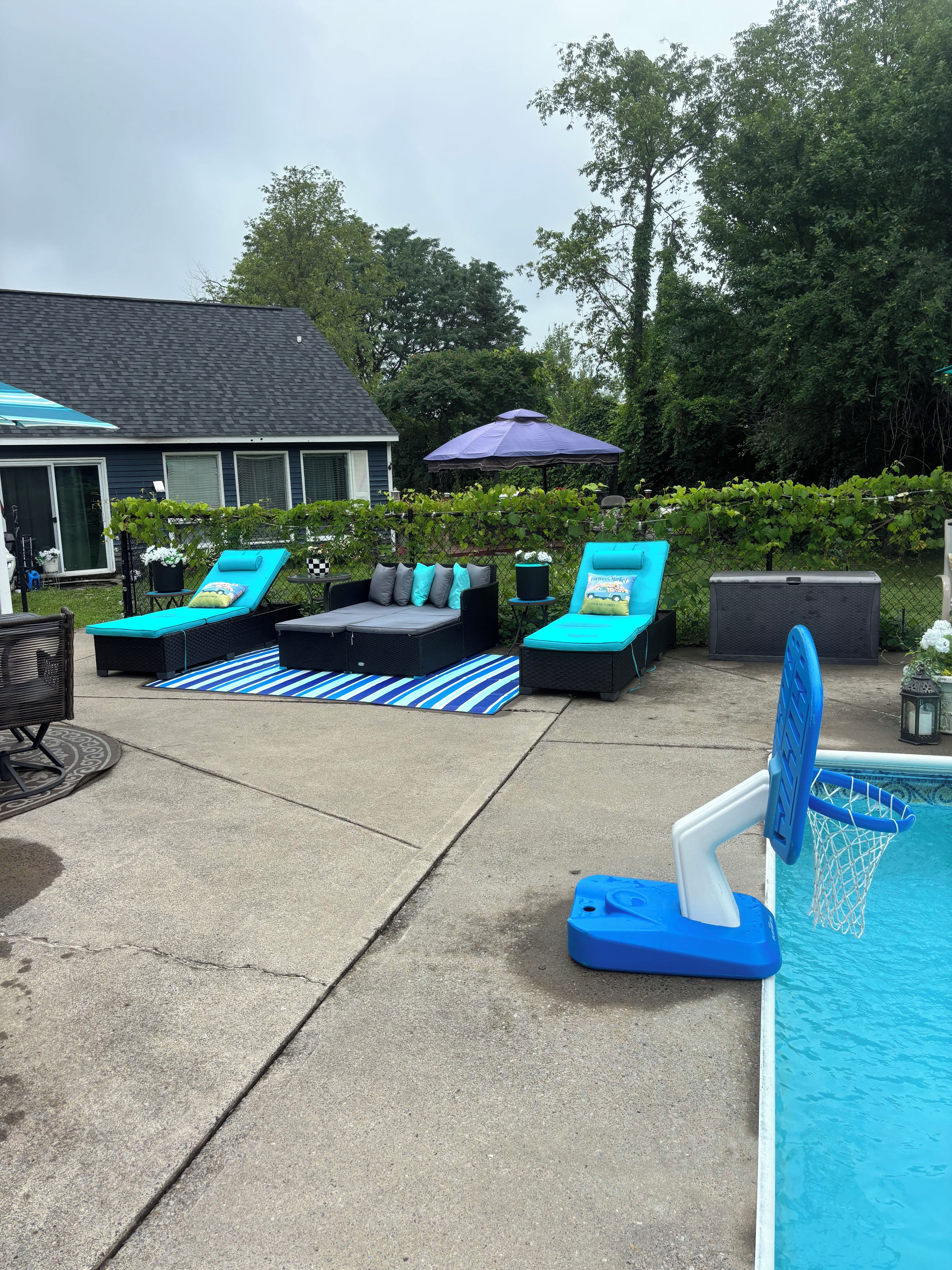 A backyard with a swimming pool, lounge chairs, and a covered patio area.