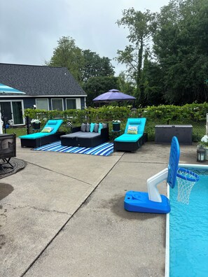 A backyard with a swimming pool, lounge chairs, and a covered patio area.