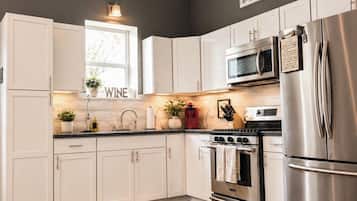 A modern kitchen with white cabinets, stainless steel appliances, and a dark wall.