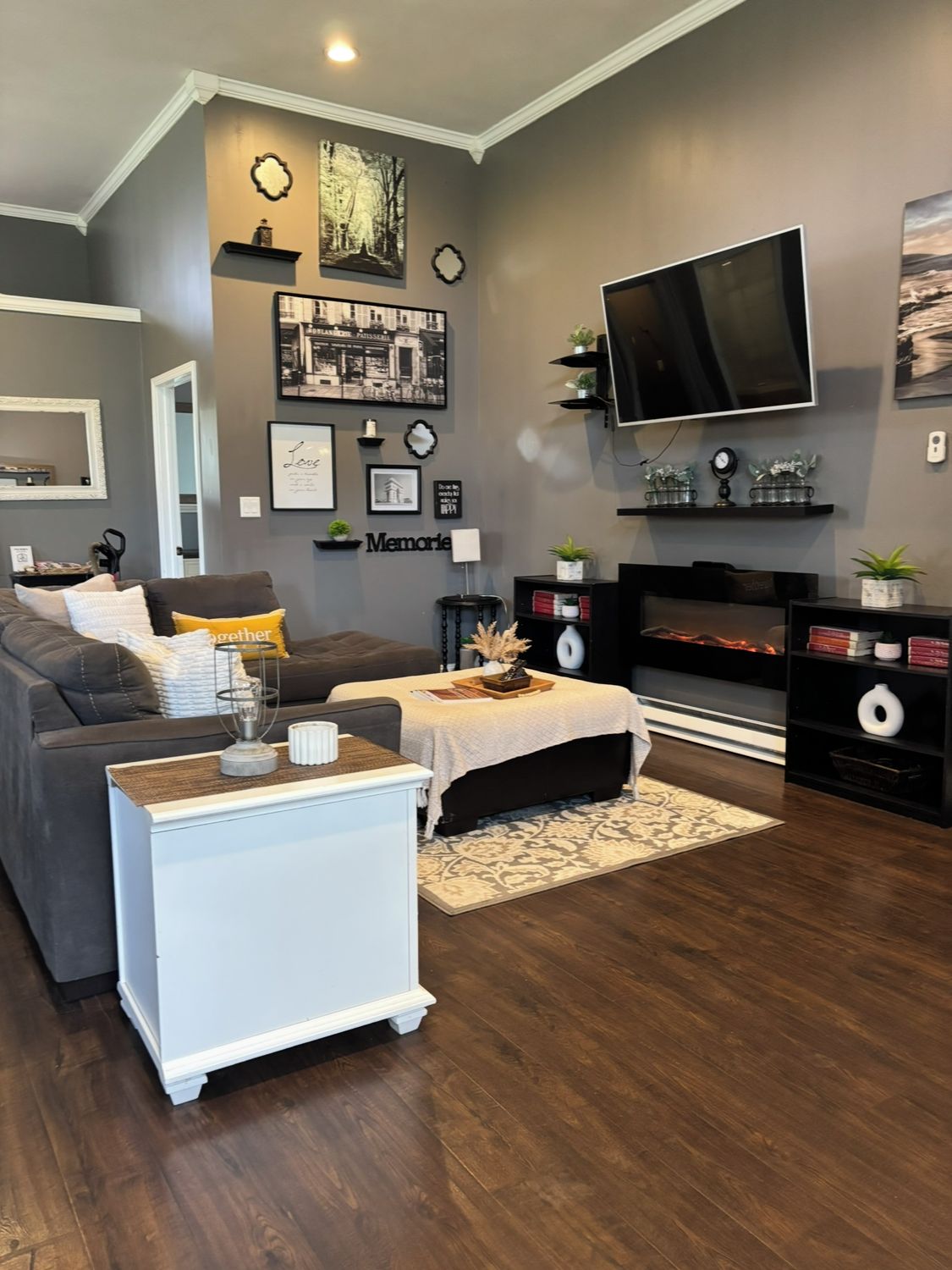 A modern living room with a grey wall, a flat-screen TV, a sofa, a coffee table, and a fireplace.