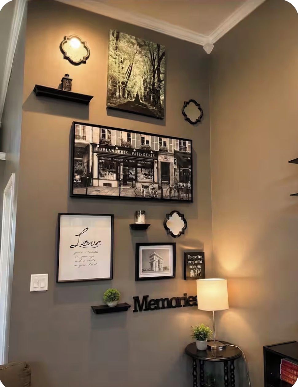 Een muur met verschillende ingekaderde foto's, een lamp en een plank met een plant.