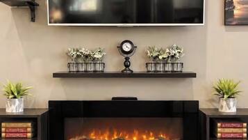 Un salón con chimenea, un televisor de pantalla plana montado sobre ella y estanterías decorativas con plantas.