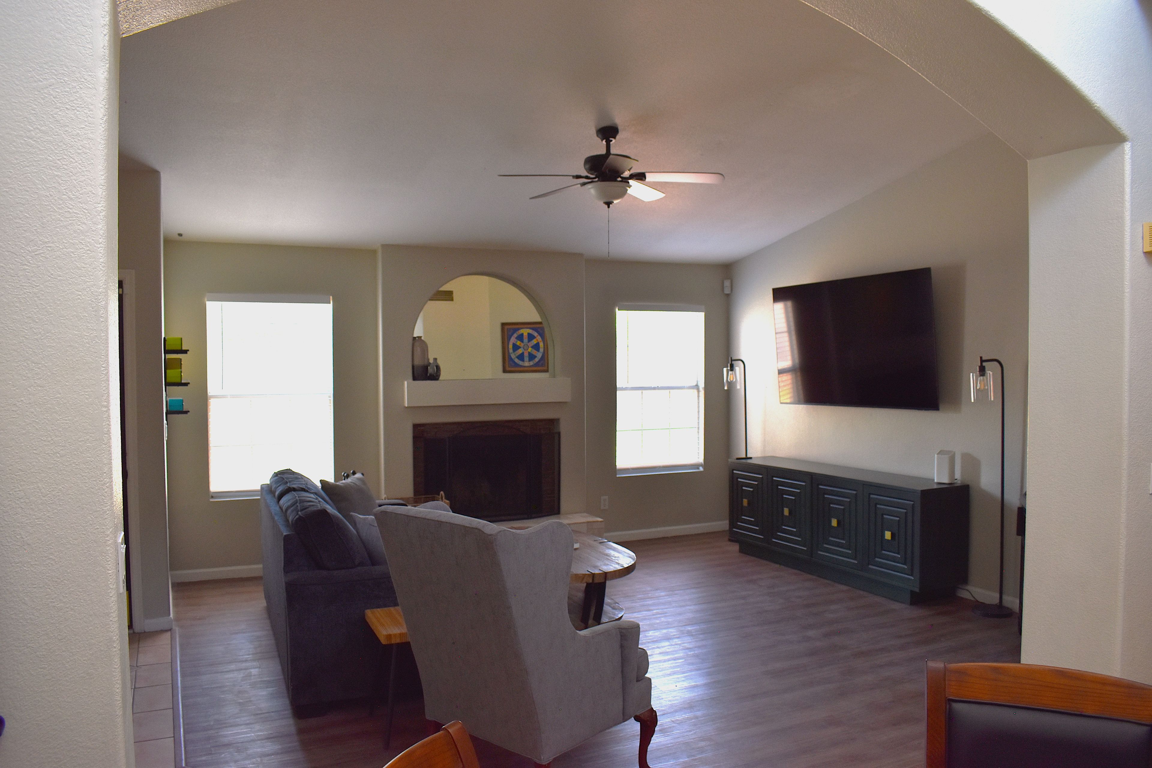 A living room with a fireplace, a ceiling fan, and a flat-screen TV mounted on the wall.