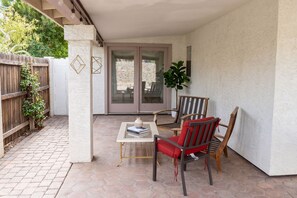 Eine Terrasse mit Tisch, zwei Stühlen, einem Blumentopf und Blick auf eine Steinmauer durch Glastüren.