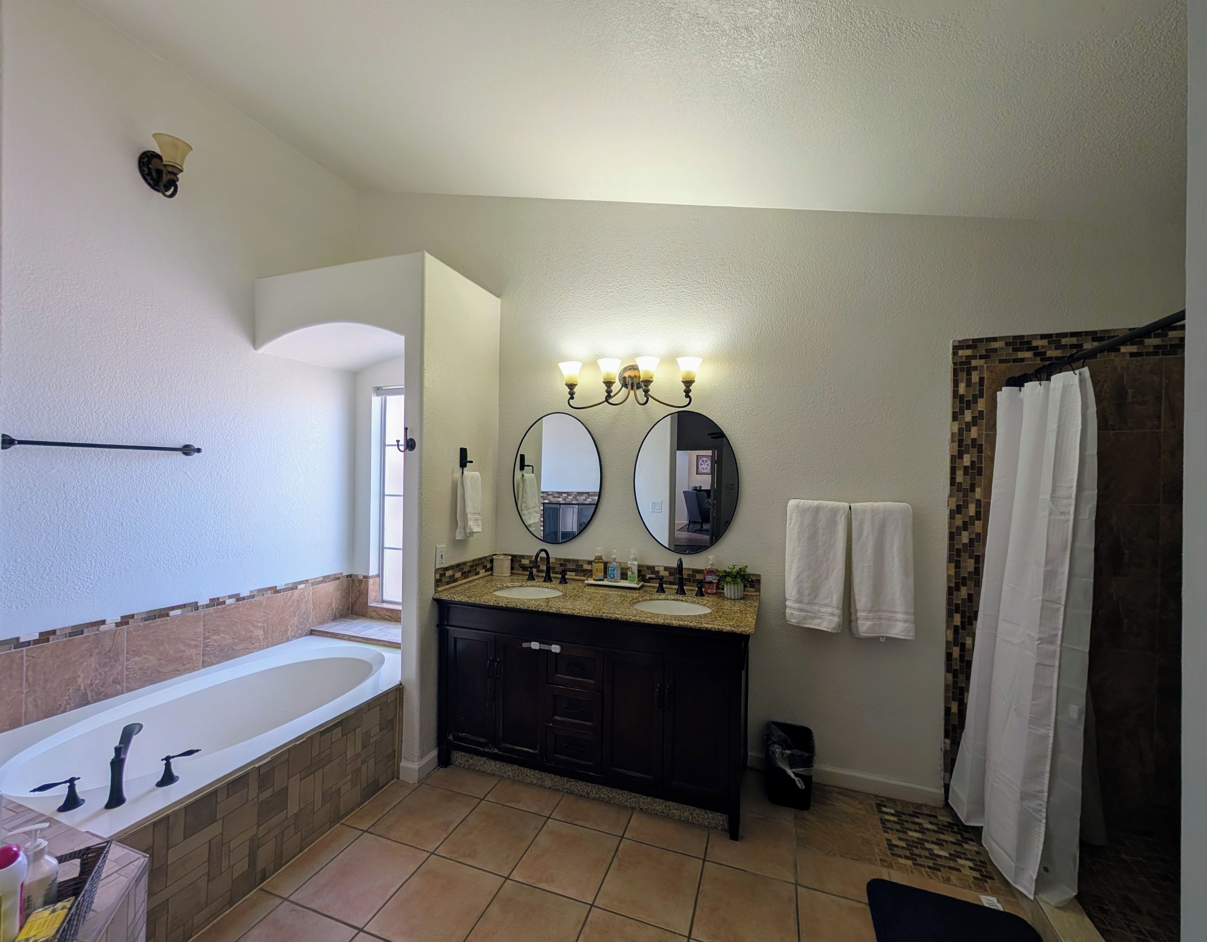 A bathroom with a bathtub, double sink vanity, two wall-mounted mirrors, and a shower curtain.