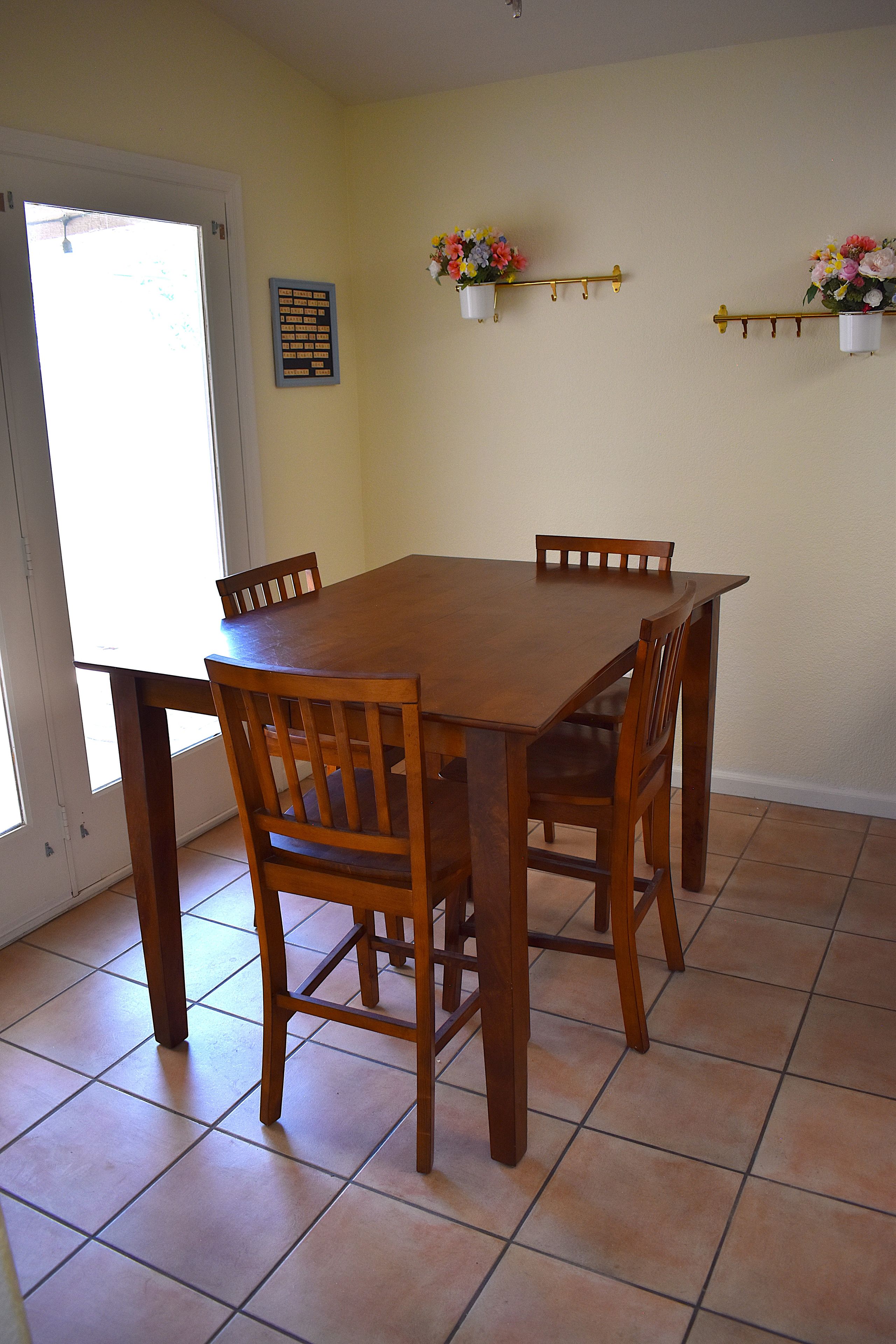 Un comedor con mesa y sillas de madera, piso de baldosas y una puerta que da al exterior.