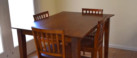 Un comedor con mesa y sillas de madera, piso de baldosas y una puerta que da al exterior.
