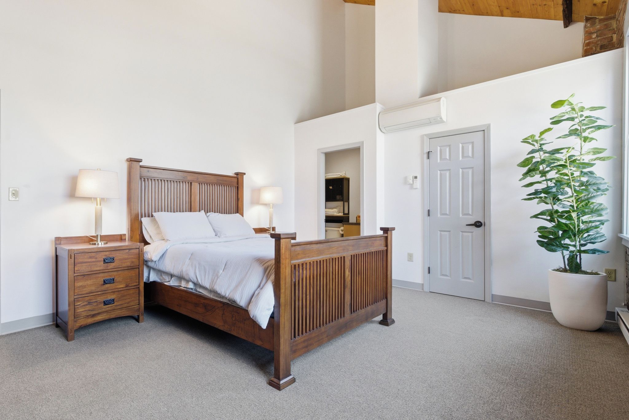 Une chambre à coucher avec un lit en bois, des tables de chevet, une commode, une plante en pot et une porte.