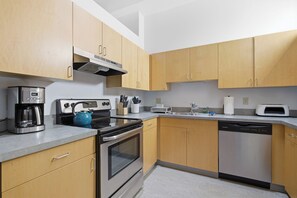 A modern kitchen with stainless steel appliances, wooden cabinets, and a grey countertop.