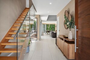 A modern interior with a wooden staircase, a glass railing, a dining area, and a kitchen with wooden cabinets.