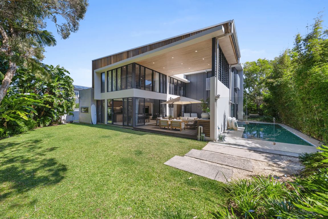 A modern two-story house with a large glass facade, a swimming pool, and a well-maintained lawn.